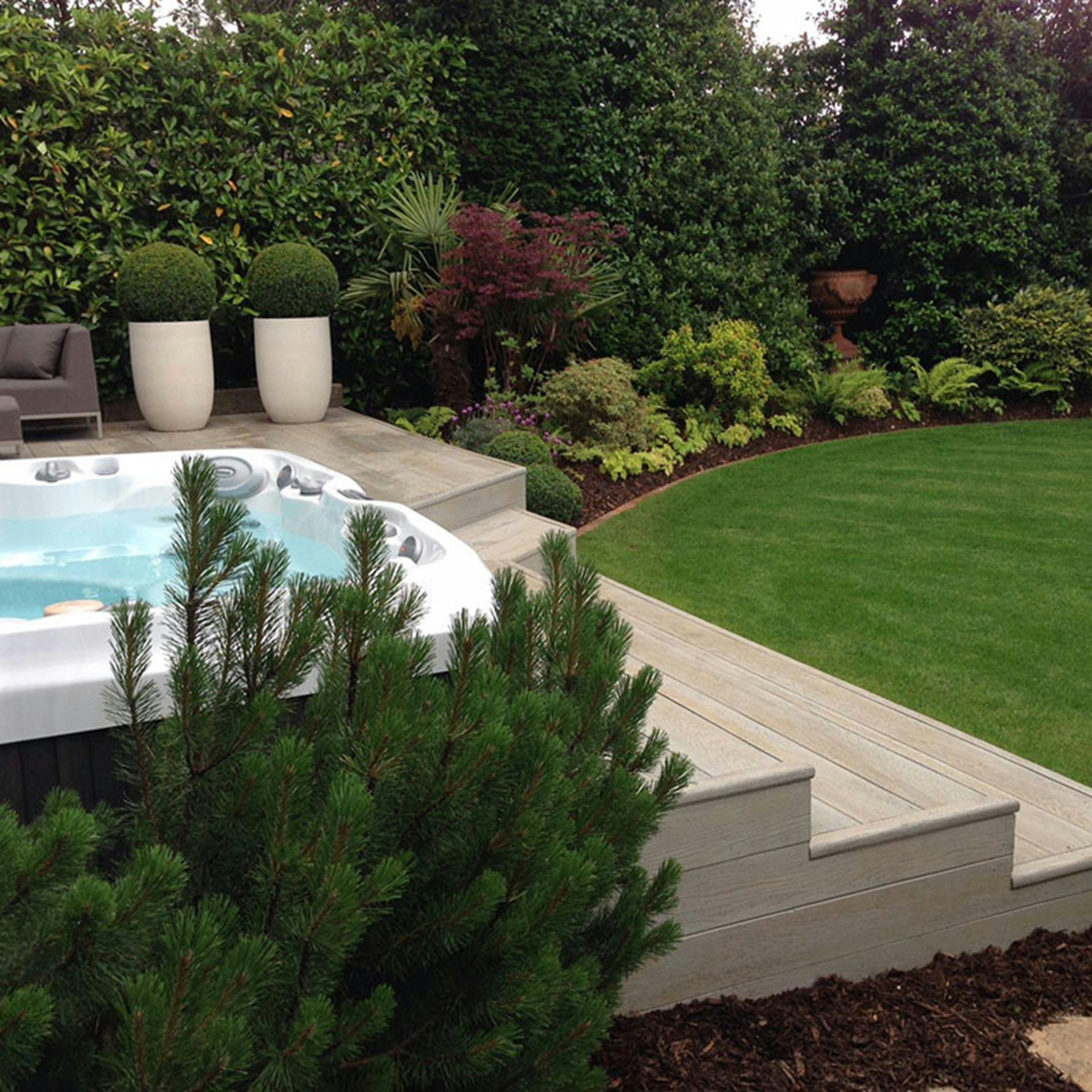 Modern hot tub on a wooden deck surrounded by lush garden landscaping